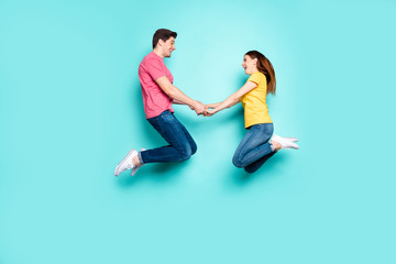 Fototapeta na wymiar Full length body size profile side view of nice attractive friendly cheerful cheery couple jumping up in air holding hands spring time isolated on bright vivid shine vibrant green turquoise background
