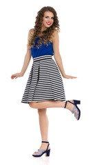 Naklejka premium Happy Young Woman In Striped Skirt And High Heels Is Standing On One Leg