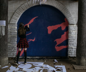 Back view of young adult female drawing bright graffiti on the wall. Modern street art concept.
