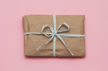 Parcel wrapping in brown craft paper and tie blue ribbon. Package. Delivery service. Online shopping. Your purchase. Gift box on a table. Isolation on pink.
