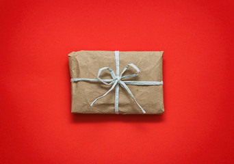 Parcel wrapping in brown craft paper and tie blue ribbon. Package. Delivery service. Online shopping. Your purchase. Gift box on a table. Isolation on red.