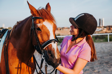 Fototapeta premium Young smiling woman standing in relax outside with wonderful chestnut horse on bridle and looking away.