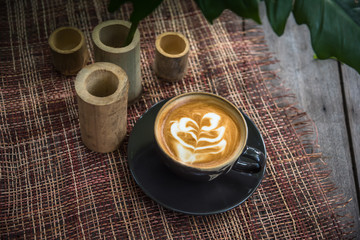 Black ceramic coffee cup on wooden table or counter with morning nature light in garden