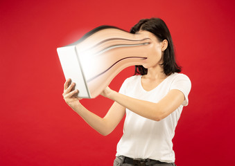 Young woman using smartphone isolated on red background. Concept of human emotions, facial...