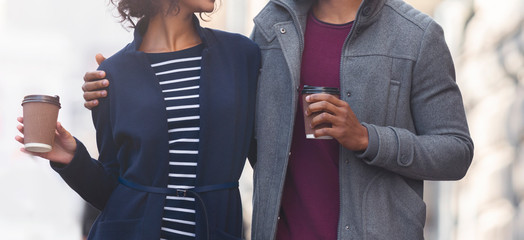 Black couple holding paper cups with coffee while walking