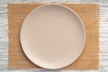 Beige round plate on a sackcloth on a wooden white table