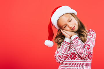 kid in sweater and santa hat sleeping isolated on red