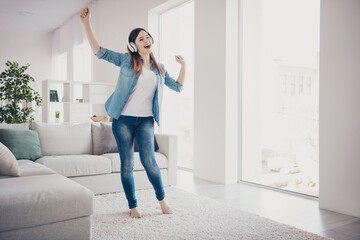 Fototapeta na wymiar Full length photo of amazing lady listening favorite melody in modern earflaps dancing overjoyed in light room wearing jeans clothes apartment indoors
