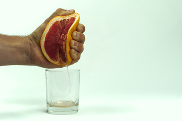 man squeezing half of juicy grapefruit to empty glass on white background, close up