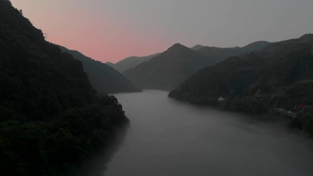 Time lapse of flying over a foggy river with a pink sky and between mountains. DongJiang Lake area, near ChenZhou, China.