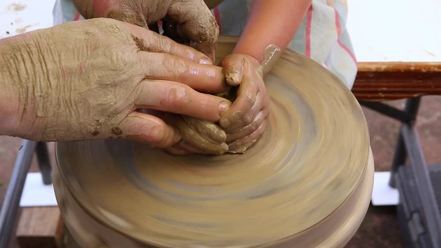 Experienced potter teaches small kid to use pottery wheel