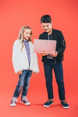 full length view of smiling kids using laptop on red
