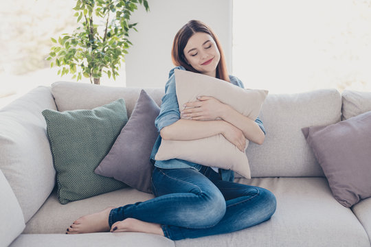 Photo of pretty lady holding big pillow close to chest closing eyes glad get rest after hard working week sitting sofa wearing jeans clothes apartment indoors