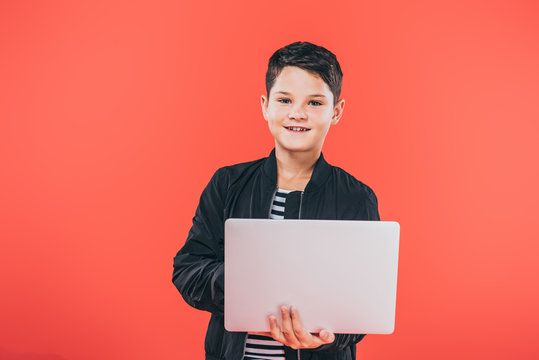 Front View Of Smiling Kid In Jacket Using Laptop Isolated On Red