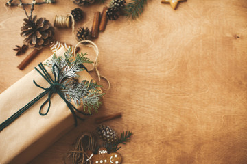 Stylish rustic christmas gifts box with cedar branch on  rural wooden table with pine cones,...