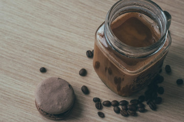Close up shot of espresso in glass mug standing on table top with roasted coffee beans and chocolate macaroon