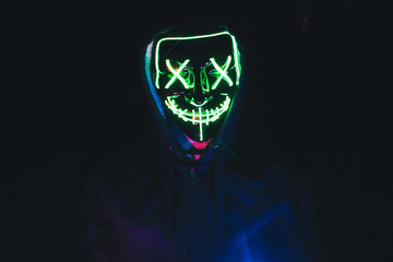 Portrait of young male wearing hoodie and green led light mask in the darkness