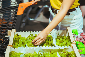 woman hand taking grapes from the box at store market