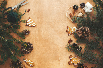 Merry Christmas flat lay. Stylish rustic frame of pine branches, cones, gingerbread cookies,thread, cinnamon, anise on rural wooden table. Space text. Seasons greeting card frame mockup