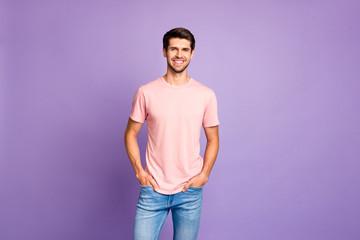 Portrait of his he nice attractive lovely glad content cheerful cheery guy wearing pink tshirt holding hands in pockets enjoying life isolated over violet purple lilac pastel color background