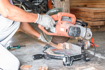 Close up of carpenter hand wearing safety glove cutting a timber woods with compound miter or angle saw in workshop place.