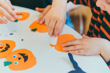 young mother with toddler son making craft pumpkins for halloween holiday