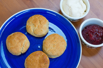 Scones on a blue plate with jam and cream in pots for afternoon tea. April 2019.