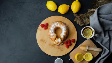 Słodka babka leżąca na drewnianej desce z owocami. Herbata z cytryną. Ciemne tło, widok z góry. Miejsce na tekst. © PhotoHunter
