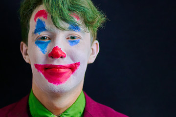 Man in mime makeup cosplay with green hair and a red suit an orange tie and a green shirt. Clown smiles