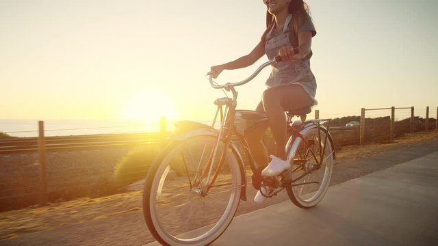 Slow motion young happy smiling girl riding bike at sunset with lens flare 