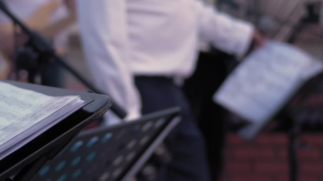 The musician in a white shirt holds a microfone and flips pages with musical notes. Out of focus Street performance.