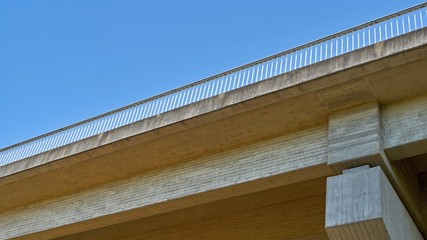 Concrete bridge with metal railing. Bottom view. Construction detail against blue sky