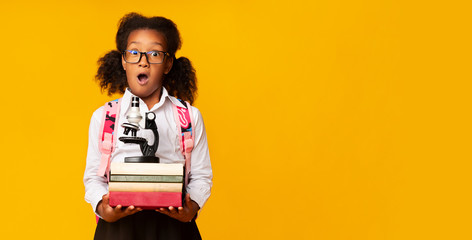 African american elementary student carrying microscope and stack of books