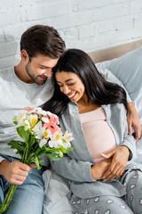 handsome man holding bouquet and hugging his smiling pregnant african american woman