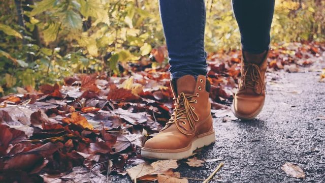 Feet in Hiking Boots Walking on Autumn Road, Close Up. SLOW MOTION 120 FPS, STABILIZED SHOT. Unrecognizable woman feet tracking on fall day outdoors, walking through woodland. Disconnected. 