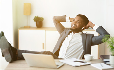 Fototapeta na wymiar Relaxed african businessman enjoy listening music in earphones at workplace