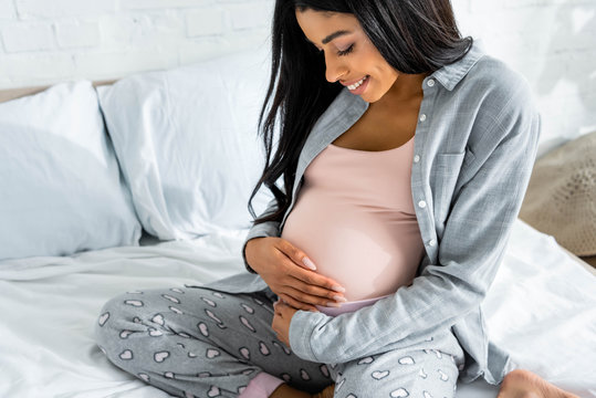 american pregnant woman in pajamas smiling and hugging belly