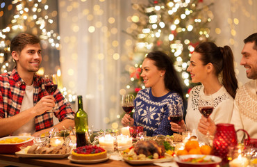 holidays and celebration concept - happy friends having christmas dinner at home and drinking red wine