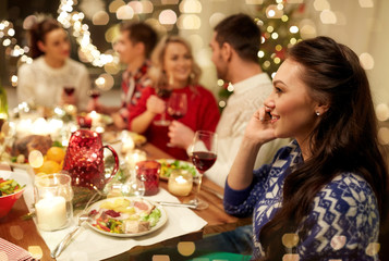 holidays, communication and celebration concept - happy young woman calling on smartphone and having christmas dinner with friends at home