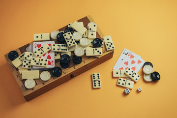 Various board games chess board, playing cards, dominoes on a orange background.