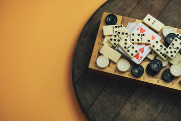 Various board games chess board, playing cards, dominoes on a old wooden table orange background.