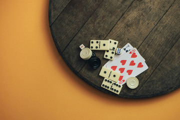 Various board games chess board, playing cards, dominoes on a old wooden table orange background.
