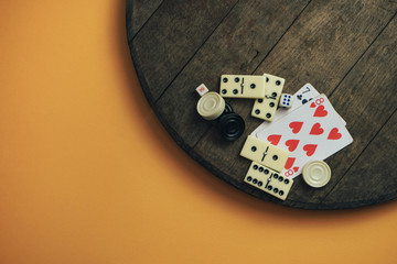 Various board games chess board, playing cards, dominoes on a old wooden table orange background.
