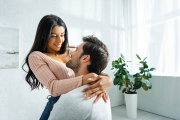Obraz premium african american woman and handsome man smiling and hugging in apartment