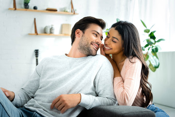 african american woman and handsome man smiling and looking at each other in apartment