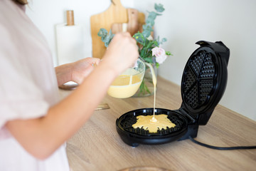 close up of woman pouring raw dough to waffle maker