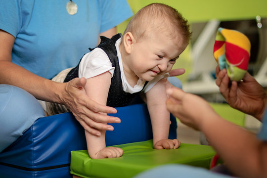 Portrait of a baby with cerebral palsy on physiotherapy in a children therapy center. Boy with disability has therapy by doing exercises. Little kid has musculoskeletal therapy in rehabitation centre.