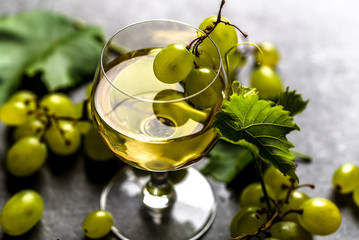 White wine glass and fresh grapes on dark background
