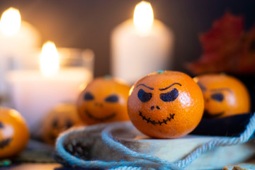 Happy Halloween citrus, tangerines painted with scary, funny faces. Dark photo with candles. Alternatives to traditional Halloween pumpkins.