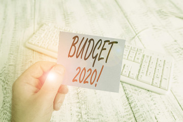Text sign showing Budget 2020. Business photo showcasing estimate of income and expenditure for next or current year man holding colorful reminder square shaped paper white keyboard wood floor